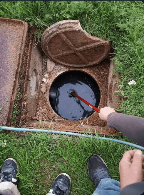 Personne sondant des eaux usées dans un regard d'égout ouvert avec un couvercle cassé.
